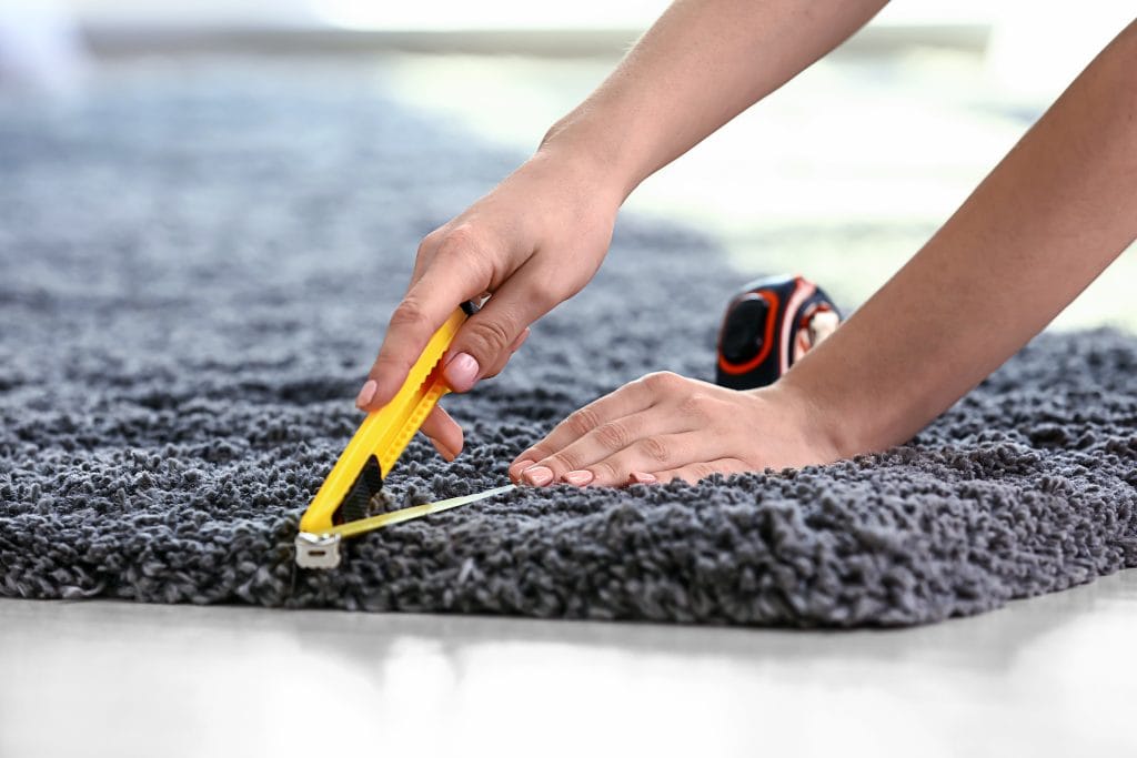 Woman With Tape Measure Cutting Carpet On Floor